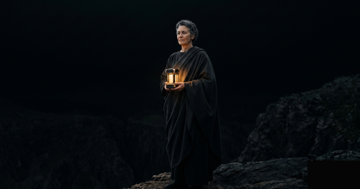 A lone figure in a dark wilderness holds the one warm gold light, calm and self-reliant